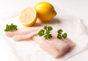 Fresh cod fish fillets with lemon and parsley on greaseproof paper